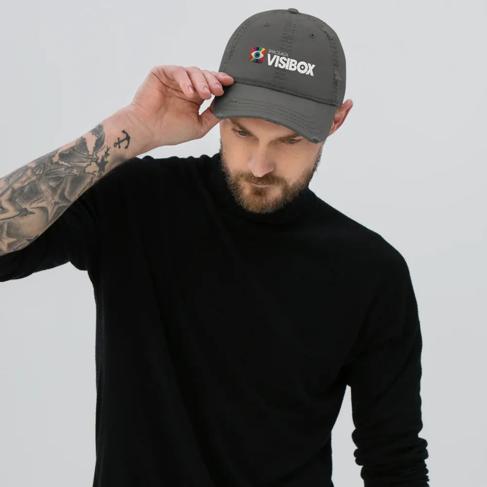Someone adjusting the charcoal grey distressed dad hat, Visibox logo embroidered on the front, frayed edges along the bill